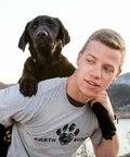 A man with a black lab puppy on his back. He is wearing an Earth Buddy t-shirt. Shop CBD apparel and CBD pet products by Earth Buddy!