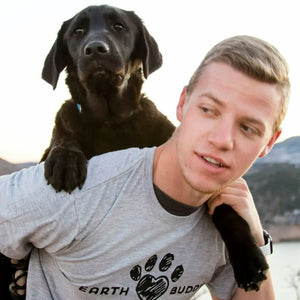 A man with a black lab puppy on his back. He is wearing an Earth Buddy t-shirt. Shop CBD apparel and CBD pet products by Earth Buddy!